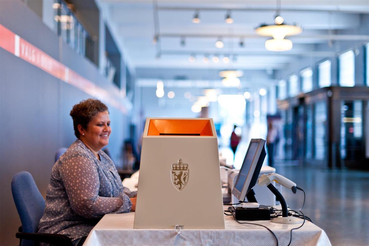 en kvinnelig valgfunksjonær sitter ved siden av en valgurne - Klikk for stort bilde
